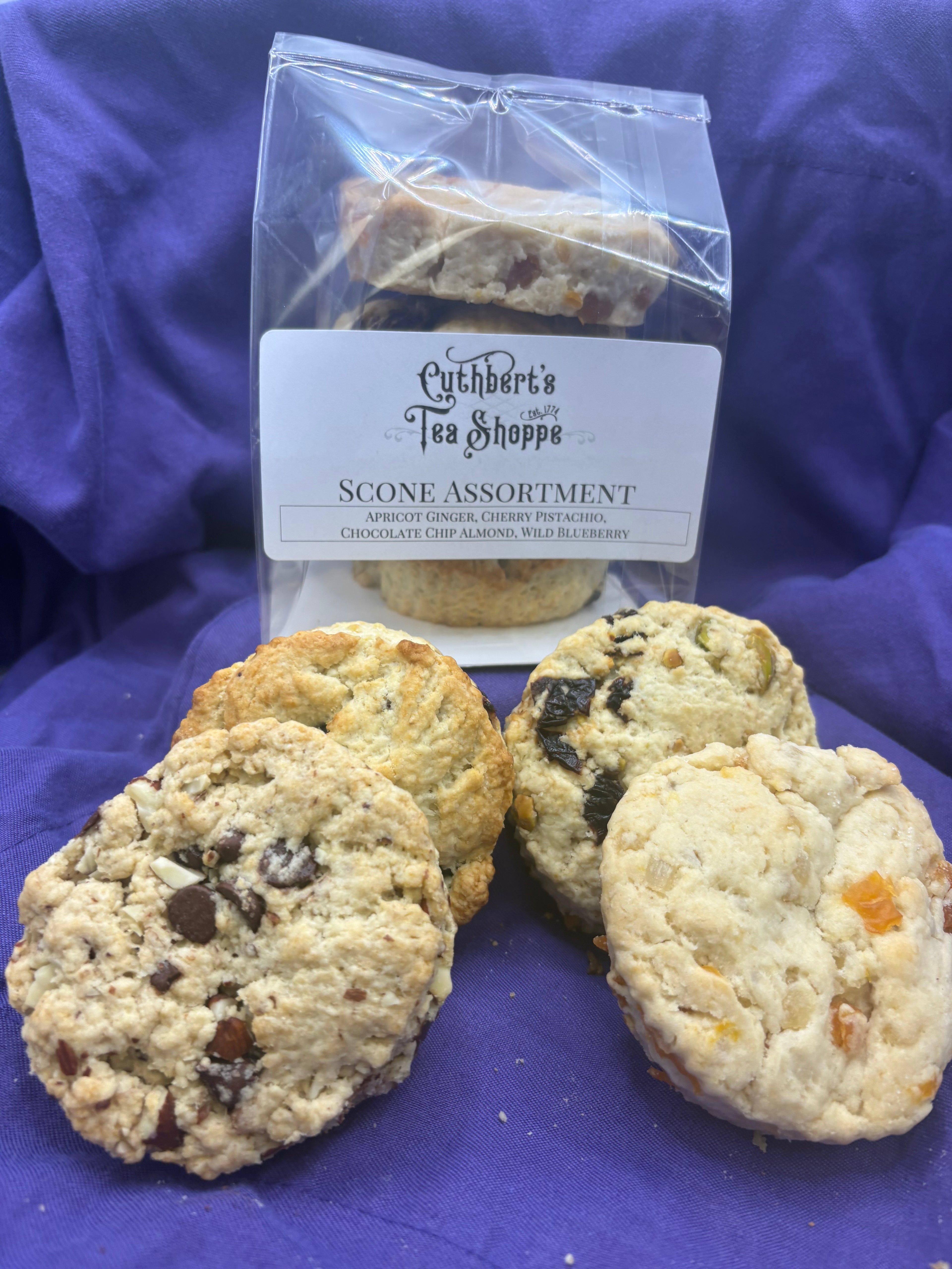 A packaged scone assortment with four individual scones set in front of it on purple fabric