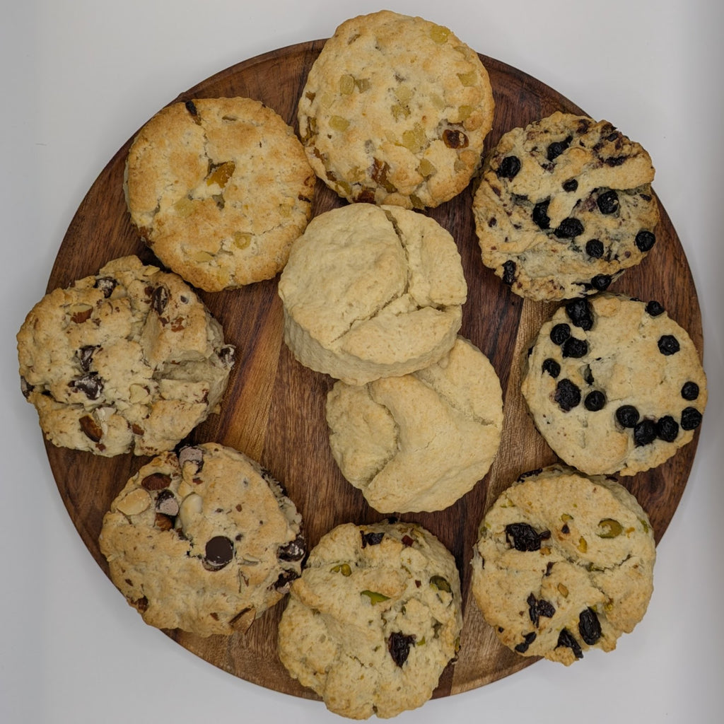 Ten assorted scones on a wooden cutting board with a white background
