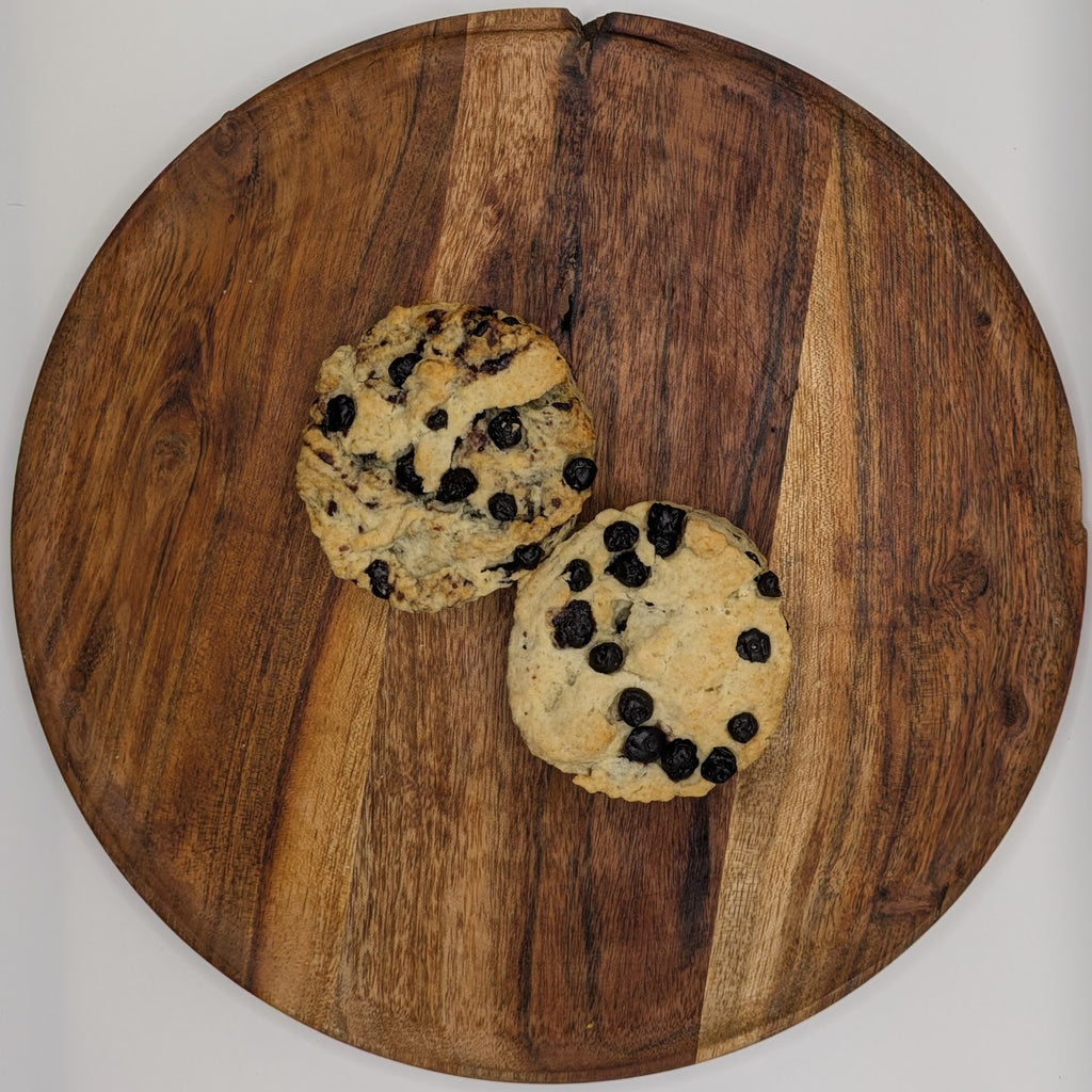 Two blueberry scones on a wooden cutting board with a white background