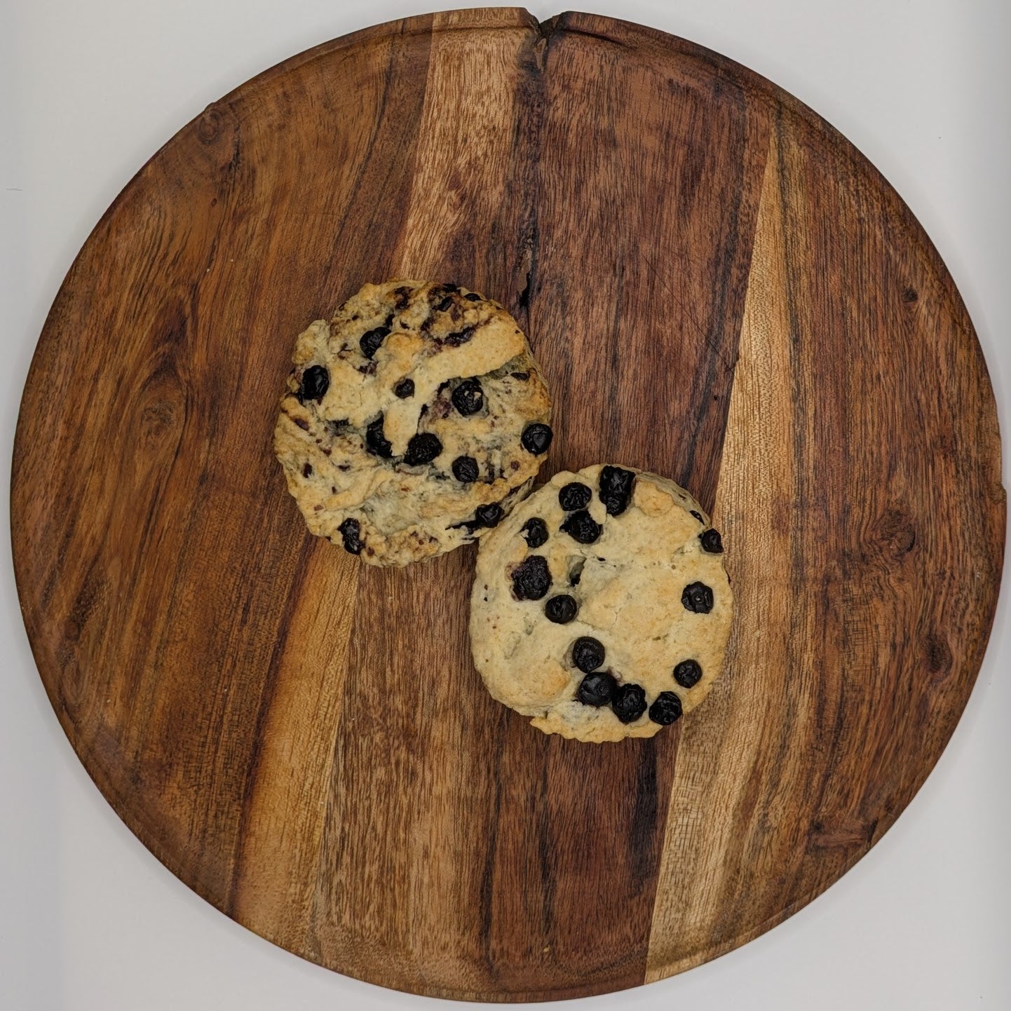 Two blueberry scones on a wooden cutting board with a white background