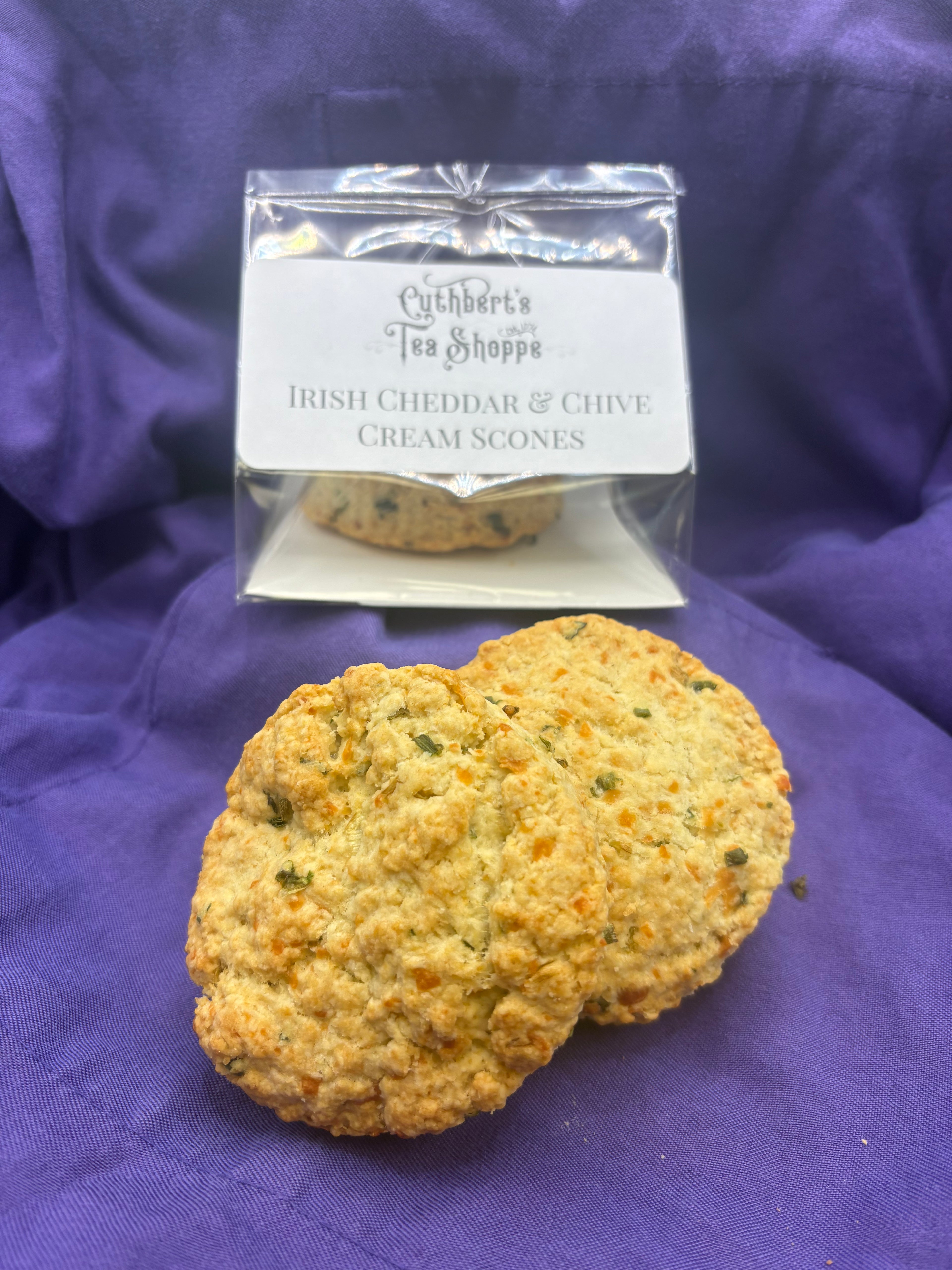 Packaged Irish cheddar and chive scones with two individual scones set in front of it on purple fabric