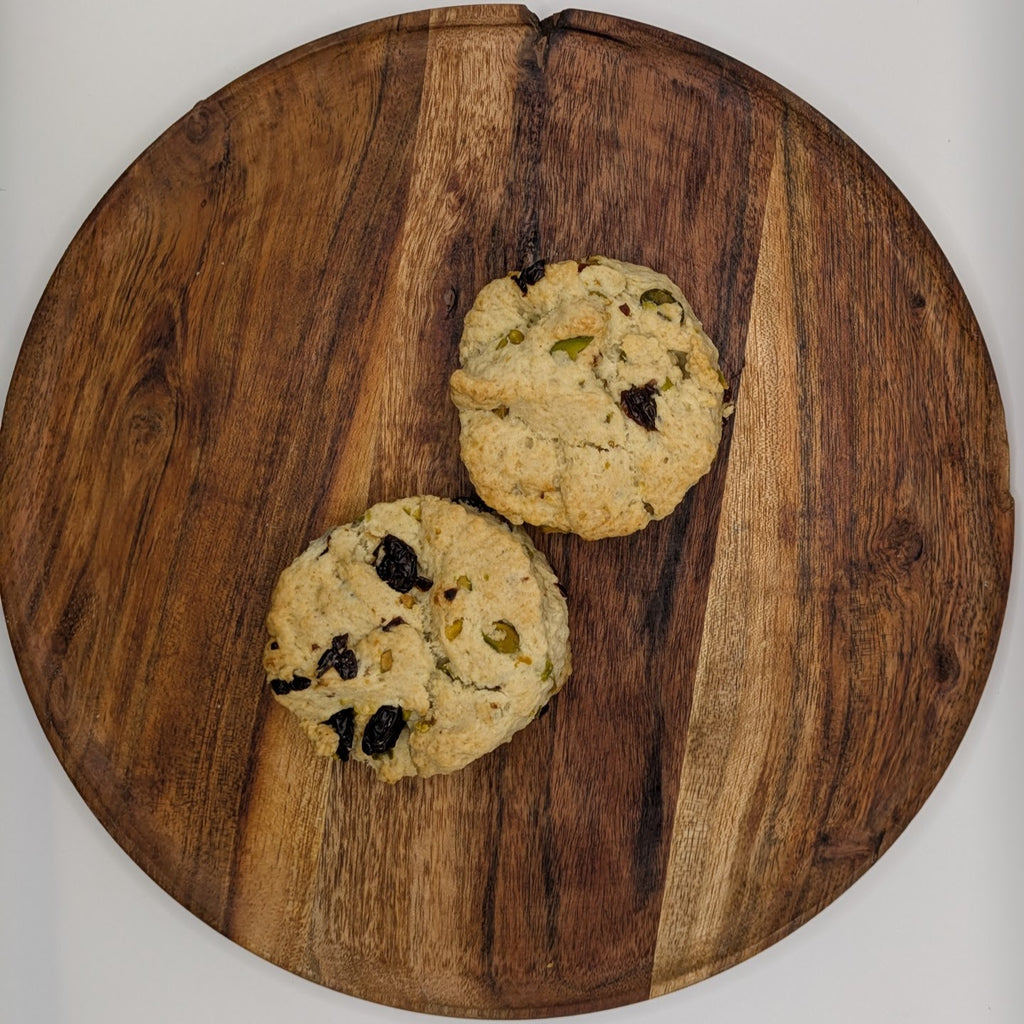 Two cherry pistachio scones on a wooden cutting board with a white background