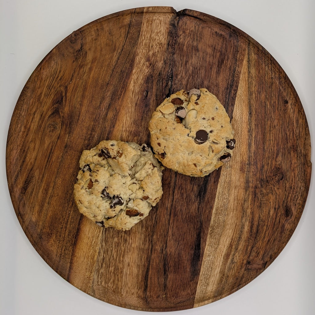 Two chocolate chip almond scones on a wooden cutting board with a white background