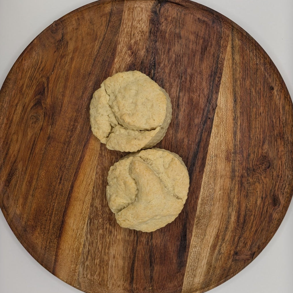 Two cream scones on a wooden cutting board with a white background