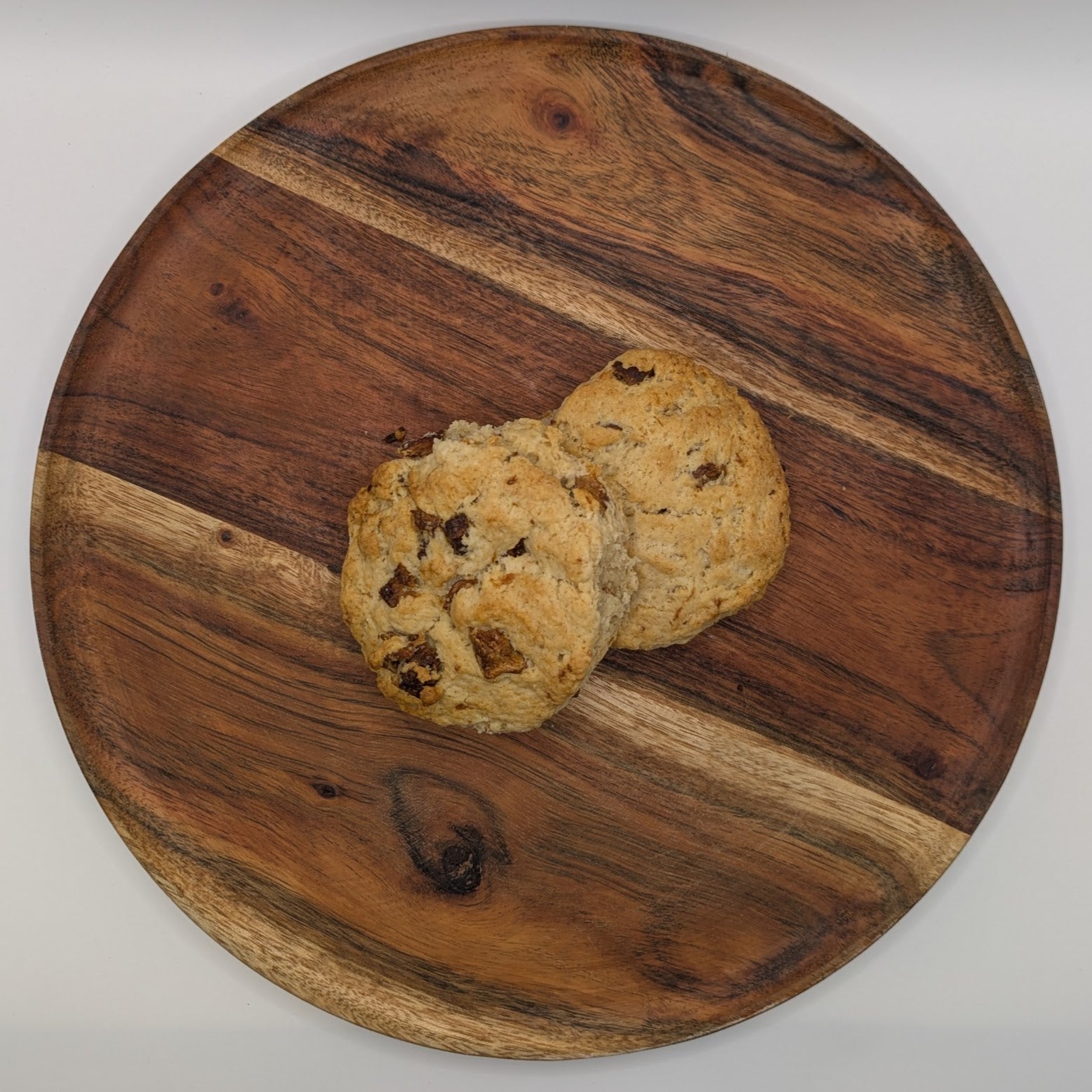 Two peaches and cream scones on a wooden cutting board with a white background